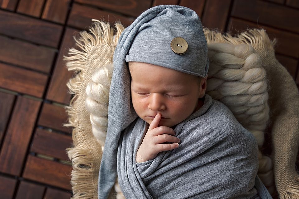 Sleeping newborn swaddled in gray fabric with decorative button detail on wooden backdrop.