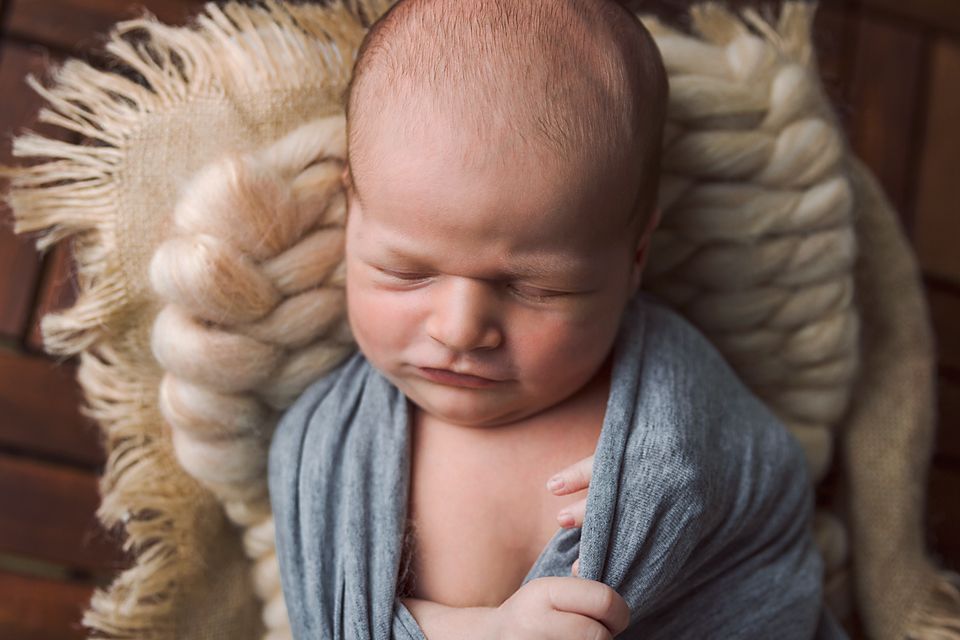 Baby sleeping peacefully on cream fur blanket while wearing gray wrap and matching cap.