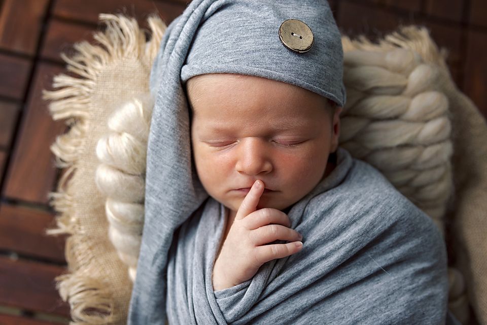 Close-up of sleeping baby in gray wrap against rustic wooden background with textured cream blanket.