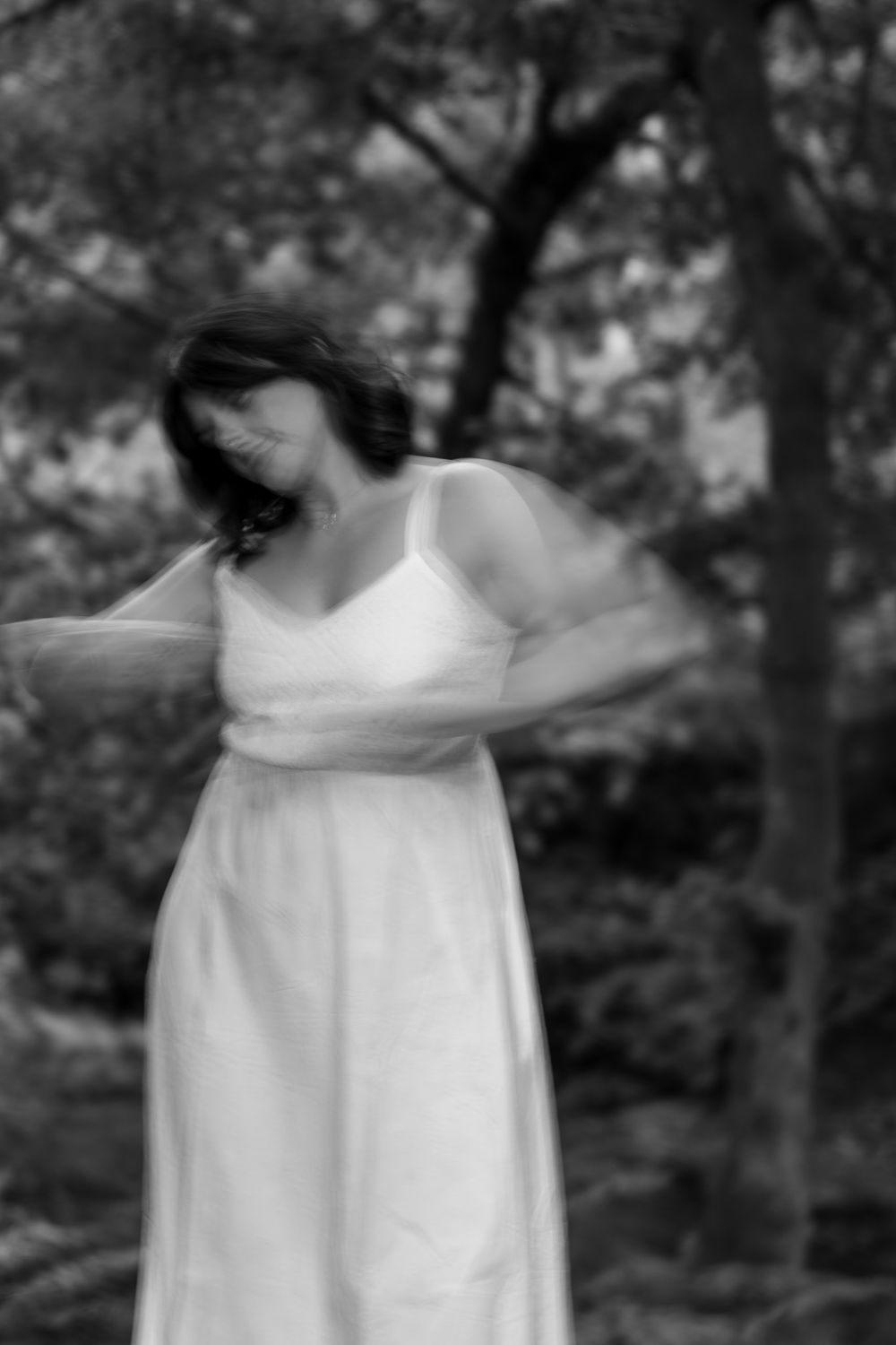 A sequence of black and white photos showing a figure in a flowing white dress moving through a forest setting.