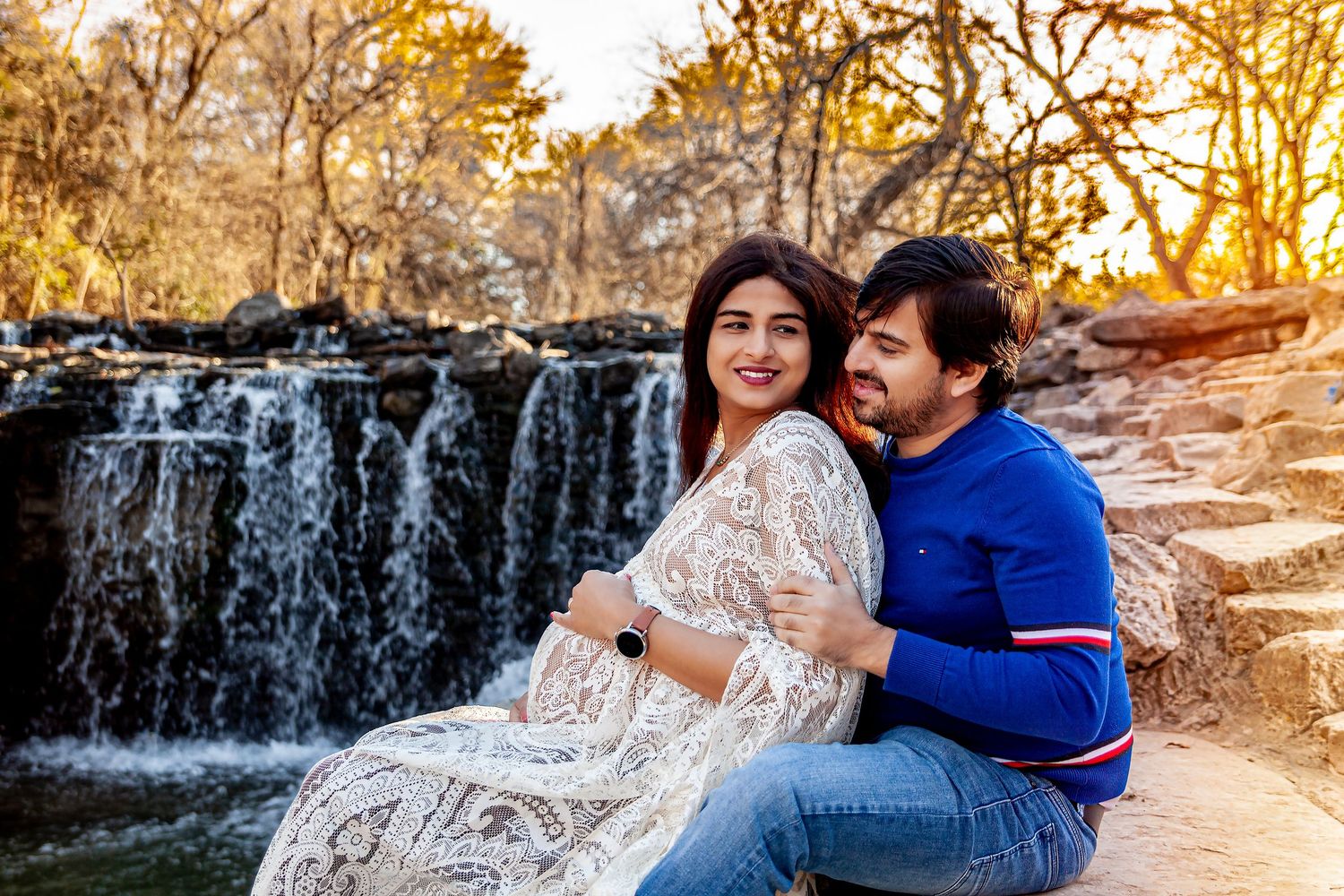 Couple posing together by scenic waterfall during sunset maternity session.