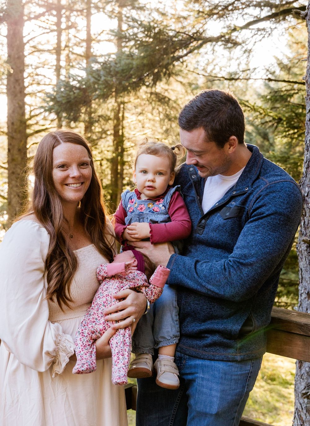 A family shares tender moments together in a sunlit forest setting during a casual outdoor photo session.