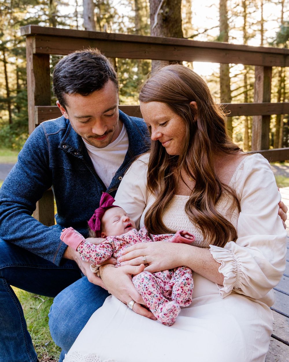 A couple sits together outdoors with their newborn baby in a cozy family moment.