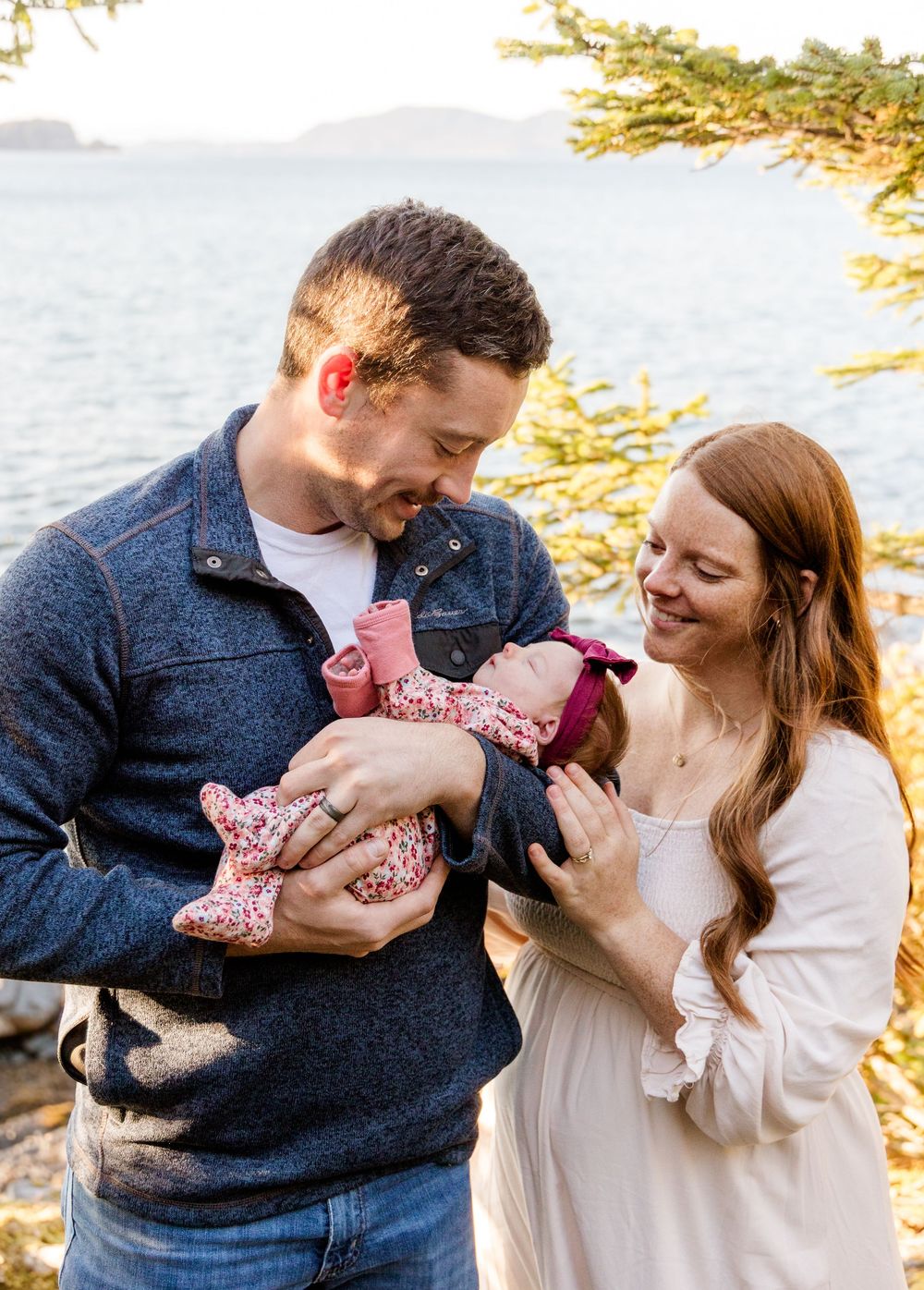 A couple shares tender moments with their baby outdoors during a sunset photoshoot by the water.