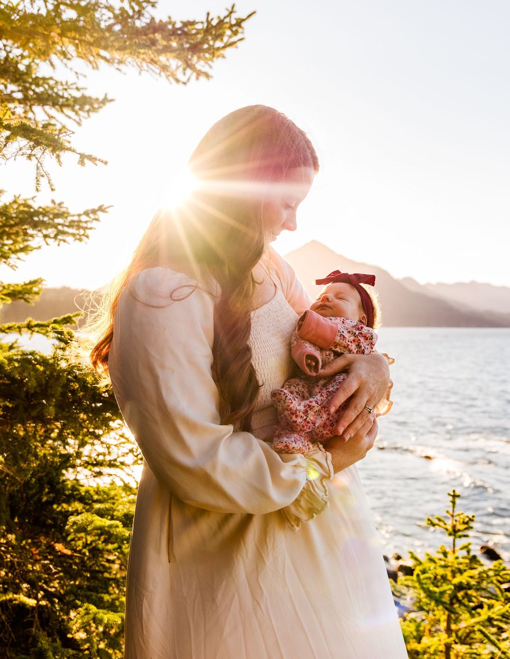 A tender moment between two people embracing at sunset with ocean and evergreen trees in the background.