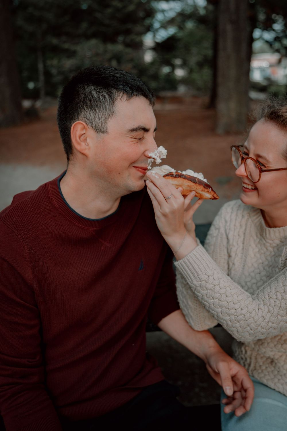 Two people share pizza and laughter while sitting together outdoors in warm autumn lighting.