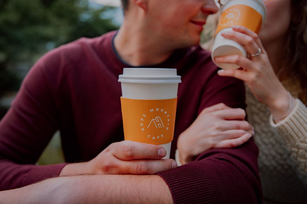 Two people holding coffee cups from a cafe share an intimate moment outdoors.