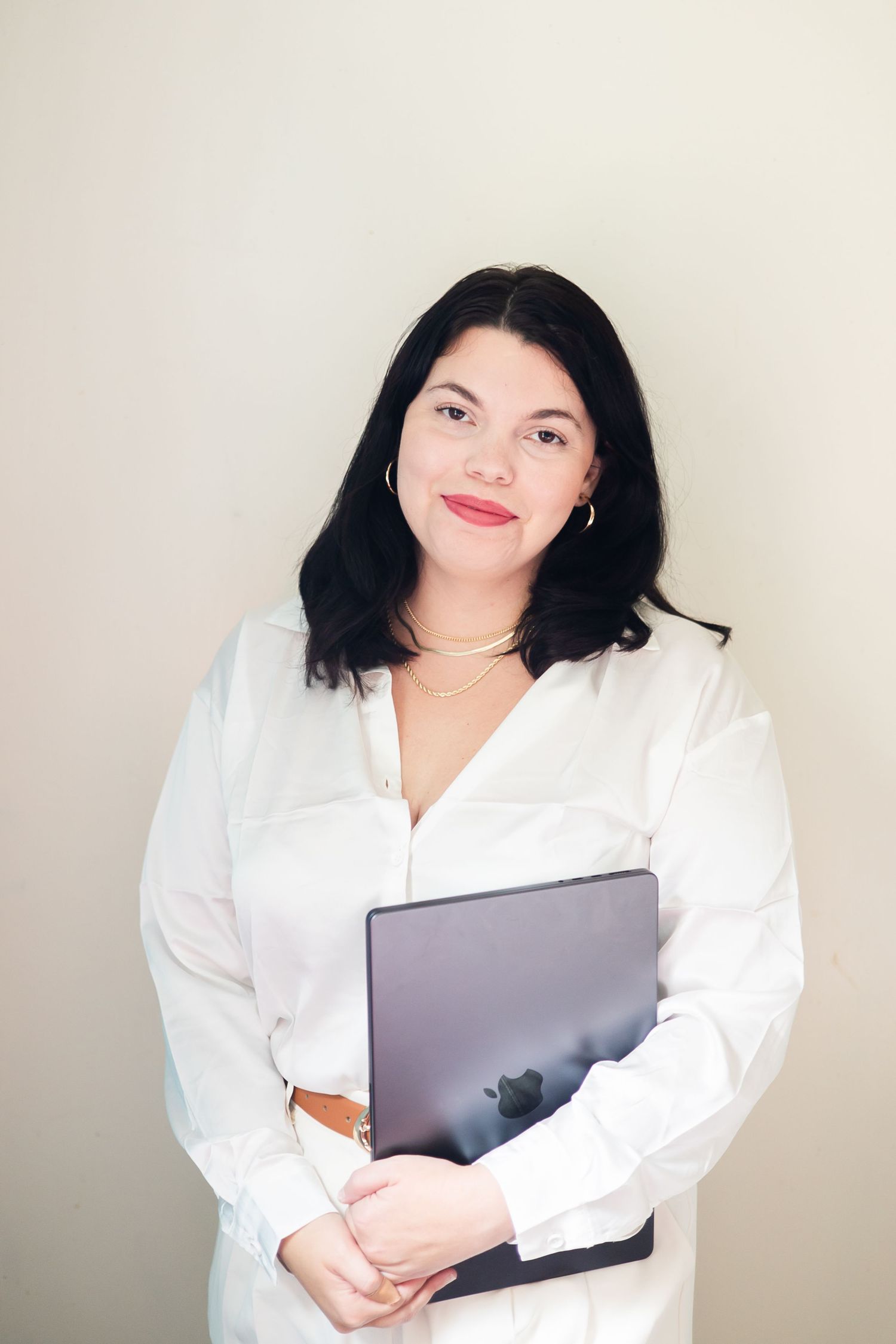 Professional photographer in morgantown wv west virginia a crisp white blouse holds a laptop while standing against a neutral wall.