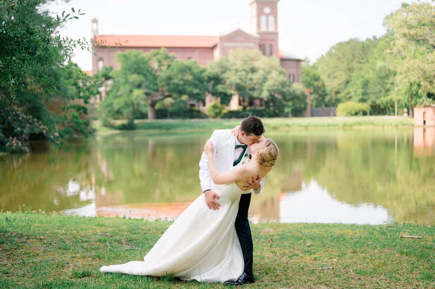 A couple shares a romantic moment by a serene lake surrounded by lush greenery on their wedding day.