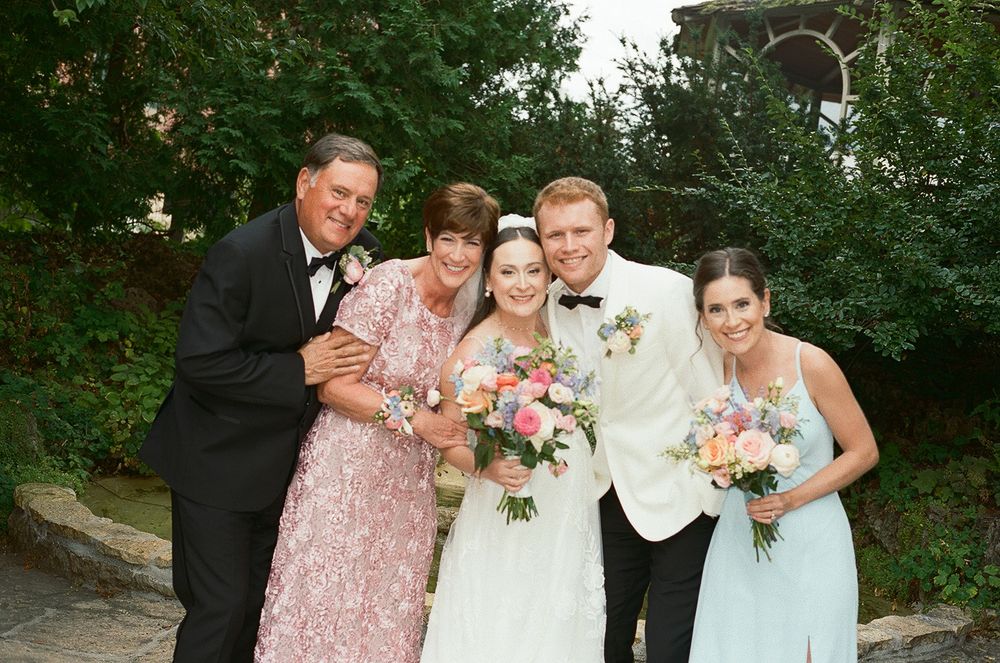 Wedding party poses together outdoors in formal attire with pink floral bouquets.