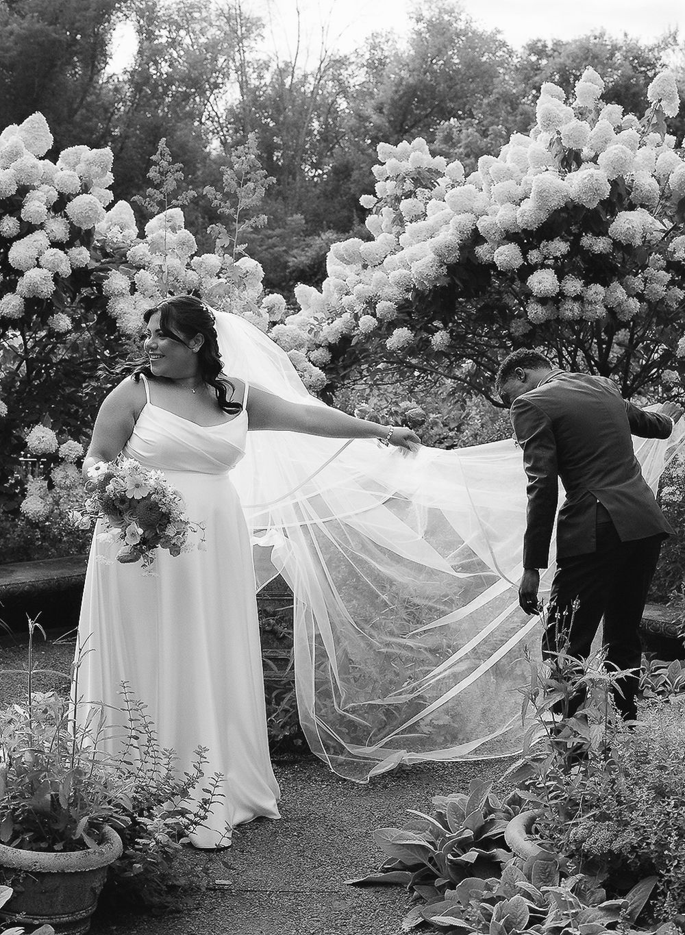 A black and white wedding photo sequence showing a flowing veil being lifted by the wind in a garden setting.