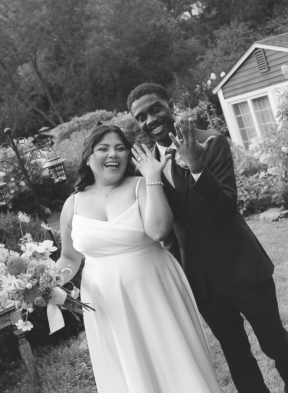 A joyful wedding couple shares a candid moment outdoors in black and white photography.