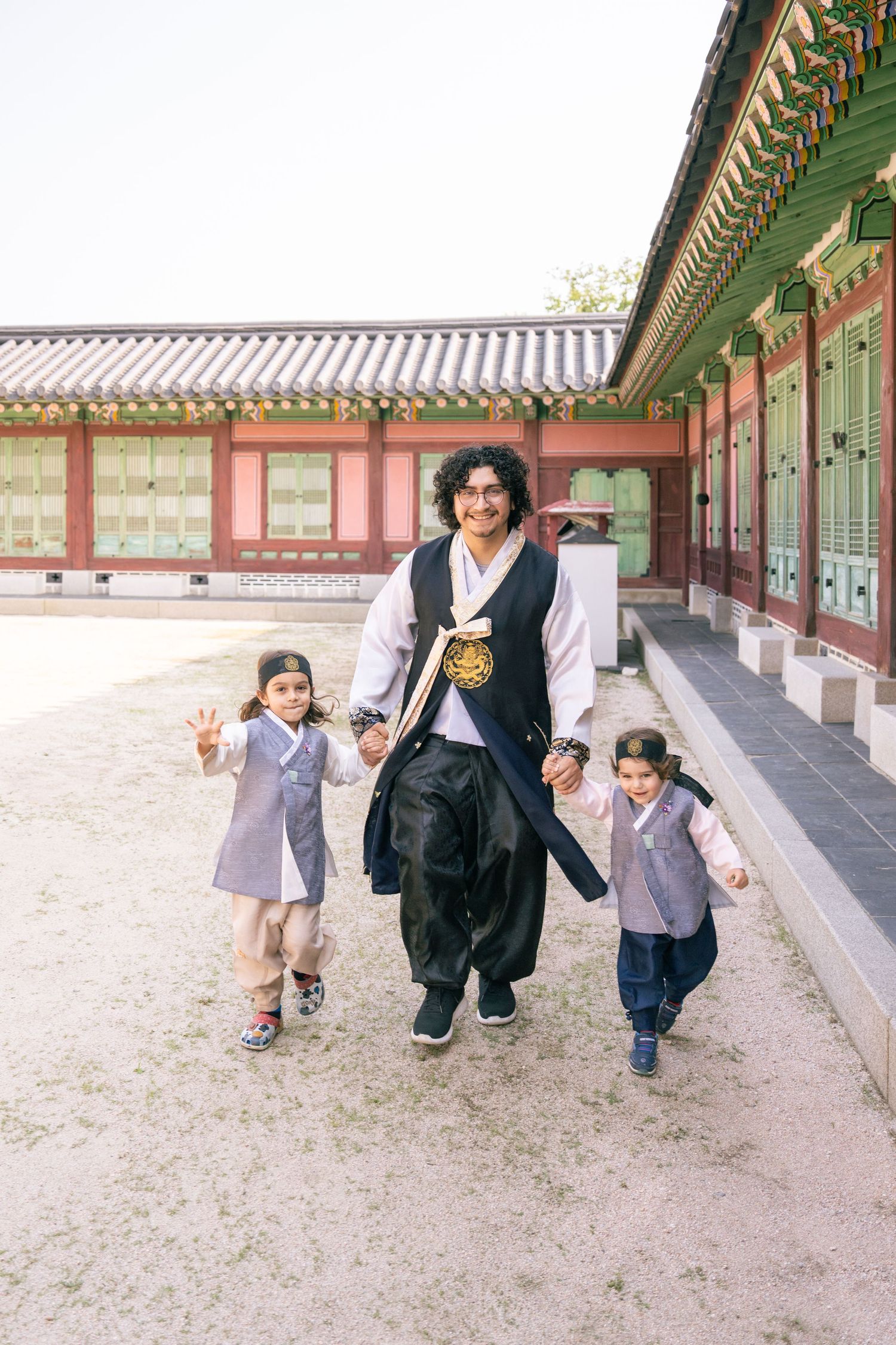 People walking and playing together along a traditional Korean palace corridor with ornate wooden architecture.
