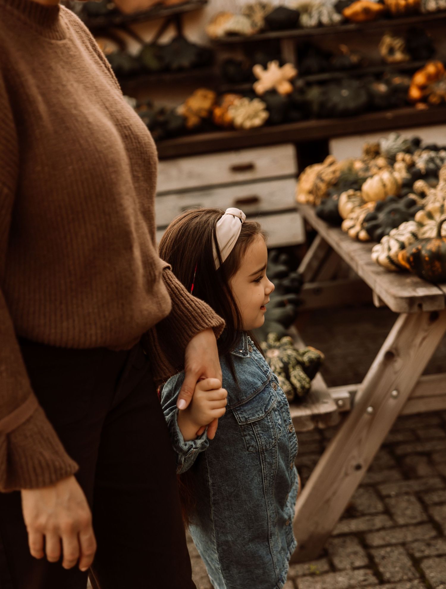 Autumn scene at rustic market with person in brown sweater among decorative displays.