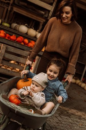 Cozy autumn scene with small children sitting in a wheelbarrow surrounded by pumpkins.