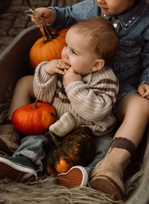 Child in knit sweater resting among autumn pumpkins and gourds.