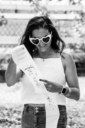 A person in a white top and jeans poses playfully with sunglasses in a black and white photo series.