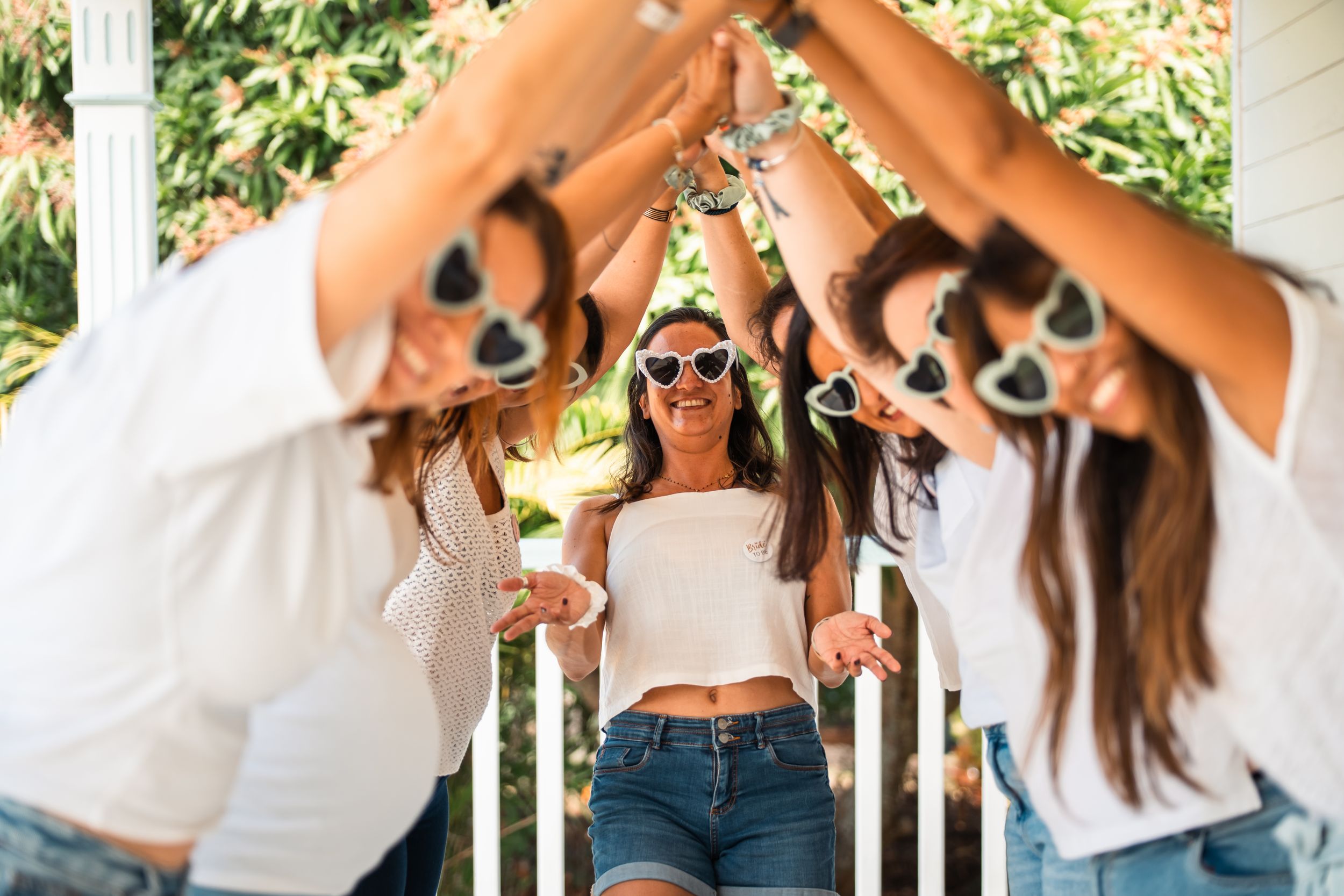 Group of friends wearing sunglasses and casual summer outfits pose playfully together outdoors.