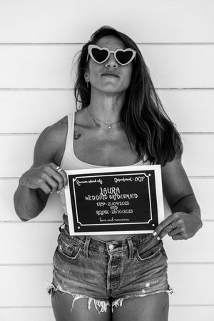 Black and white photo of person in heart sunglasses holding sign against white wall.
