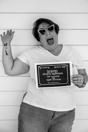 Playful black and white portraits with heart sunglasses and sign against white siding.