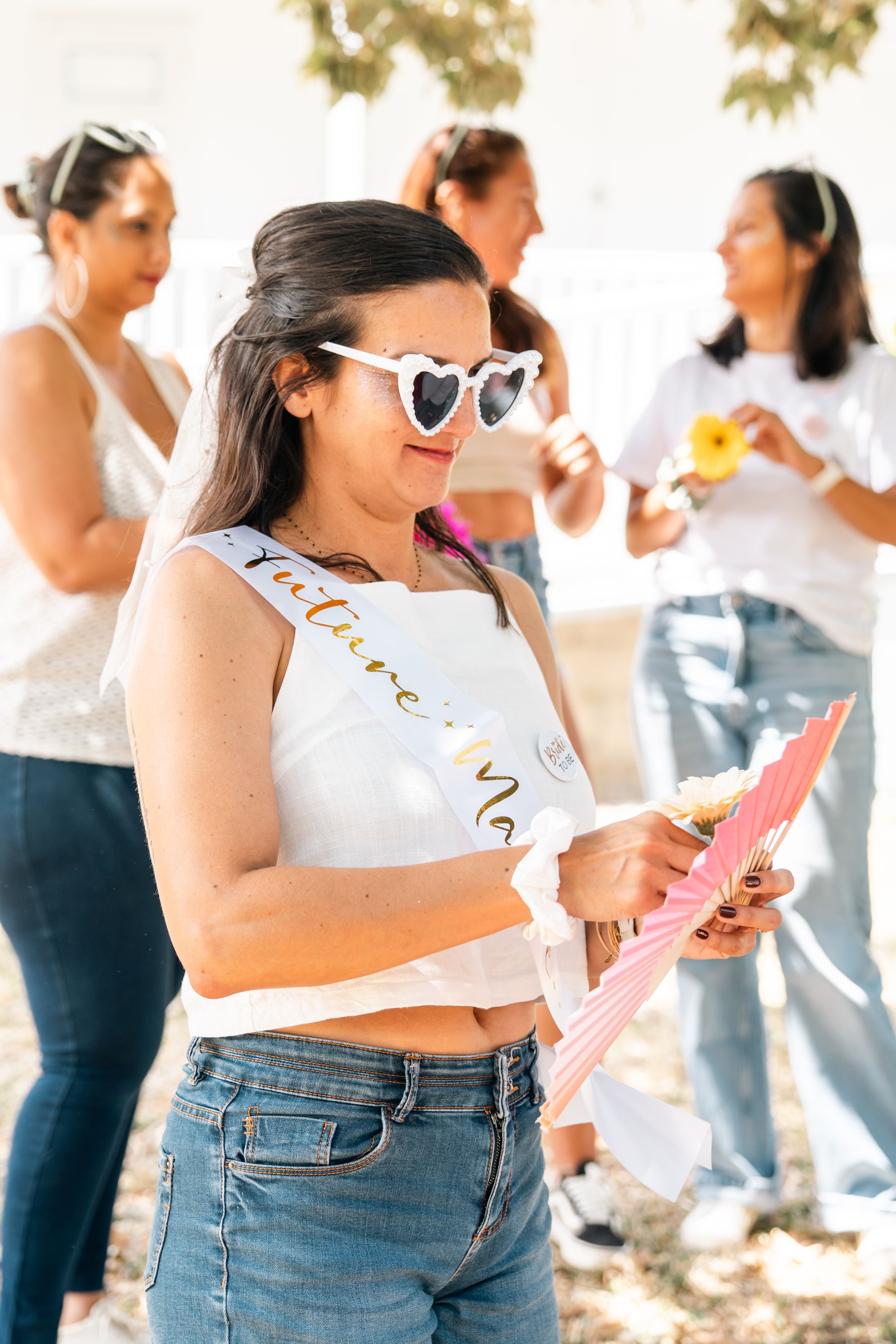 Group of women in matching white tops and jeans celebrating at an outdoor party event.