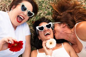 A group wearing heart-shaped sunglasses and white outfits poses playfully on grass during a summer photoshoot.