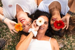 People in white clothing lying on grass in a circle formation with flowers and sunglasses.