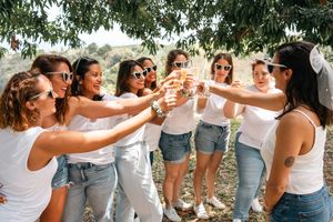 Group in white tops and jeans posing together under tree branches on sunny day.