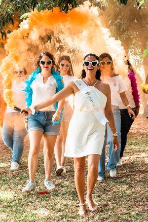Group celebrating with colorful smoke bombs while wearing sunglasses and casual summer outfits.