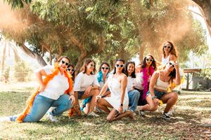 A group of friends in colorful summer outfits posing playfully on grass under trees during a sunny day.
