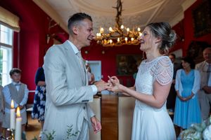 Ein formell gekleidetes Brautpaar posiert vor einem prächtigen gelben Herrenhaus mit weißen Verzierungen an ihrem Hochzeitstag.