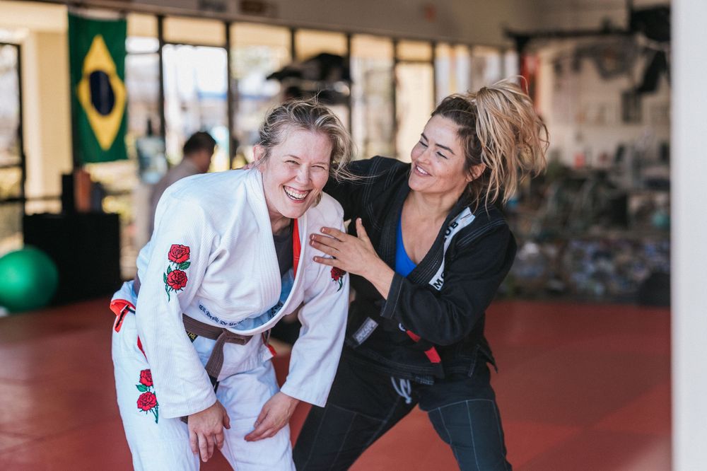 Two people in martial arts uniforms practicing grappling moves on a red mat during training.