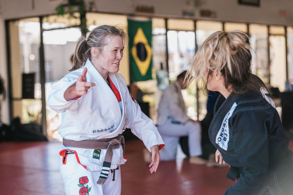 Students practice martial arts techniques with an instructor in a training studio with a Brazilian flag on the wall.