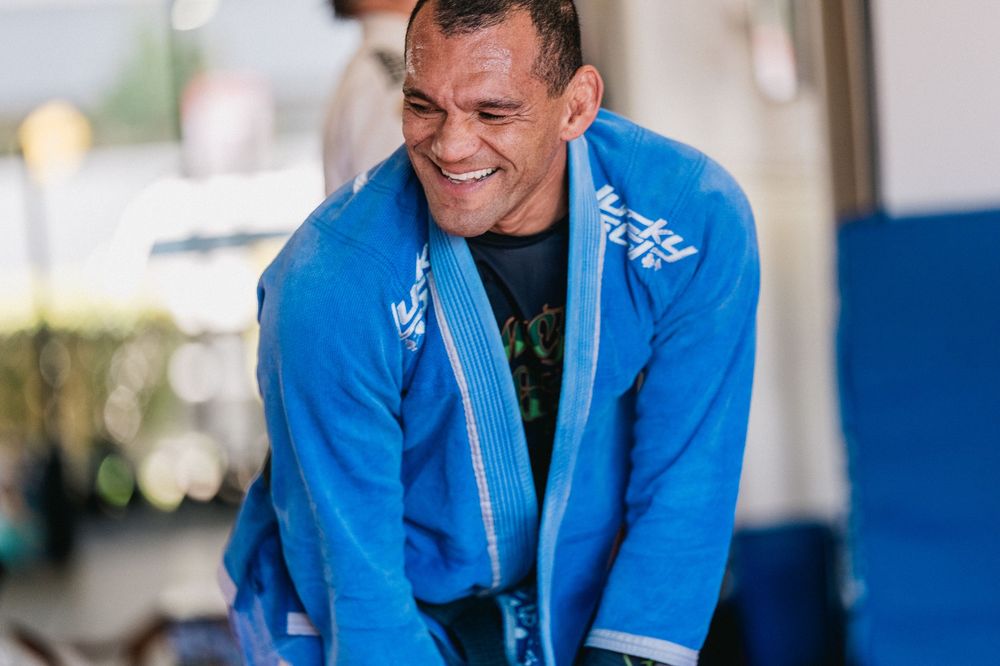 A person in a bright blue uniform jacket smiles warmly while working indoors.