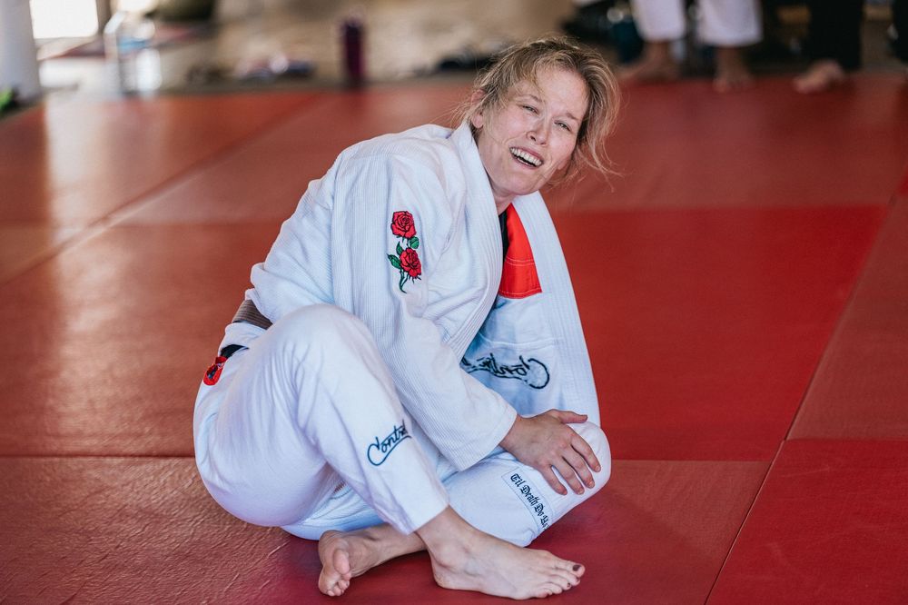 A person in a white martial arts gi uniform practicing judo or jiu-jitsu techniques on a red mat.
