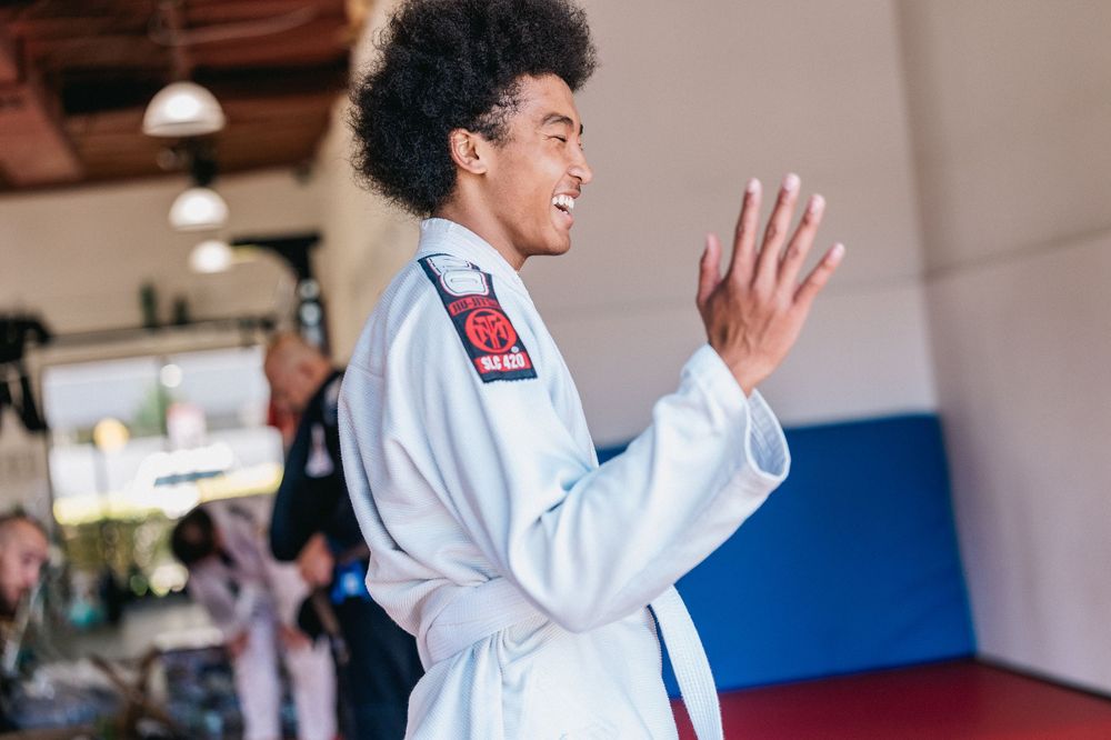 Students practicing martial arts moves in a white uniform inside a bright training studio.