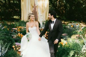 Elegant wedding couple poses in a lush garden setting with beautiful orange and yellow floral arrangements.