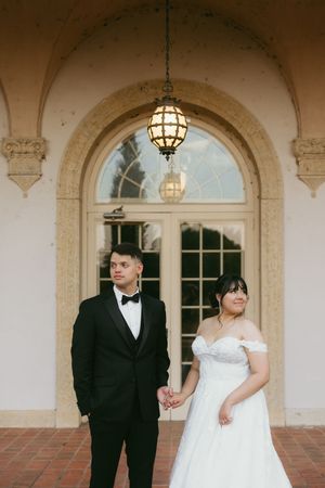 Elegant wedding couple poses under arched entryway with hanging lanterns at historic venue.