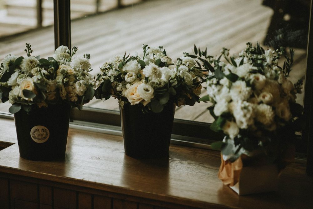 White floral arrangements in black vases line a wooden window ledge in moody lighting.