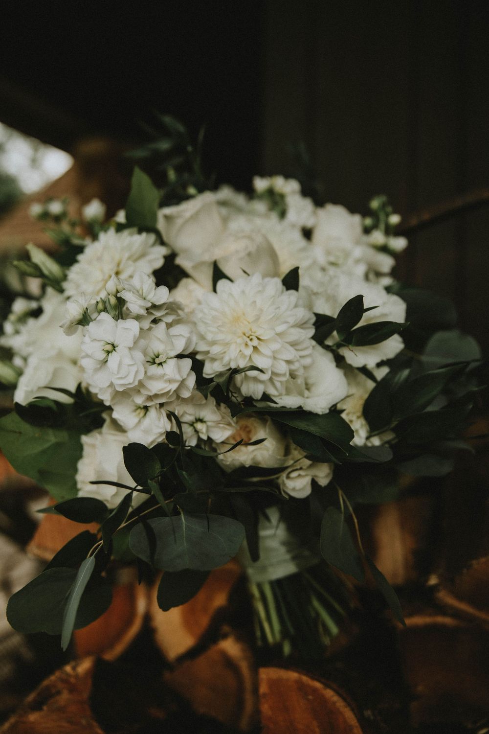 White carnation flowers arranged with dark green leaves against a moody dark background.