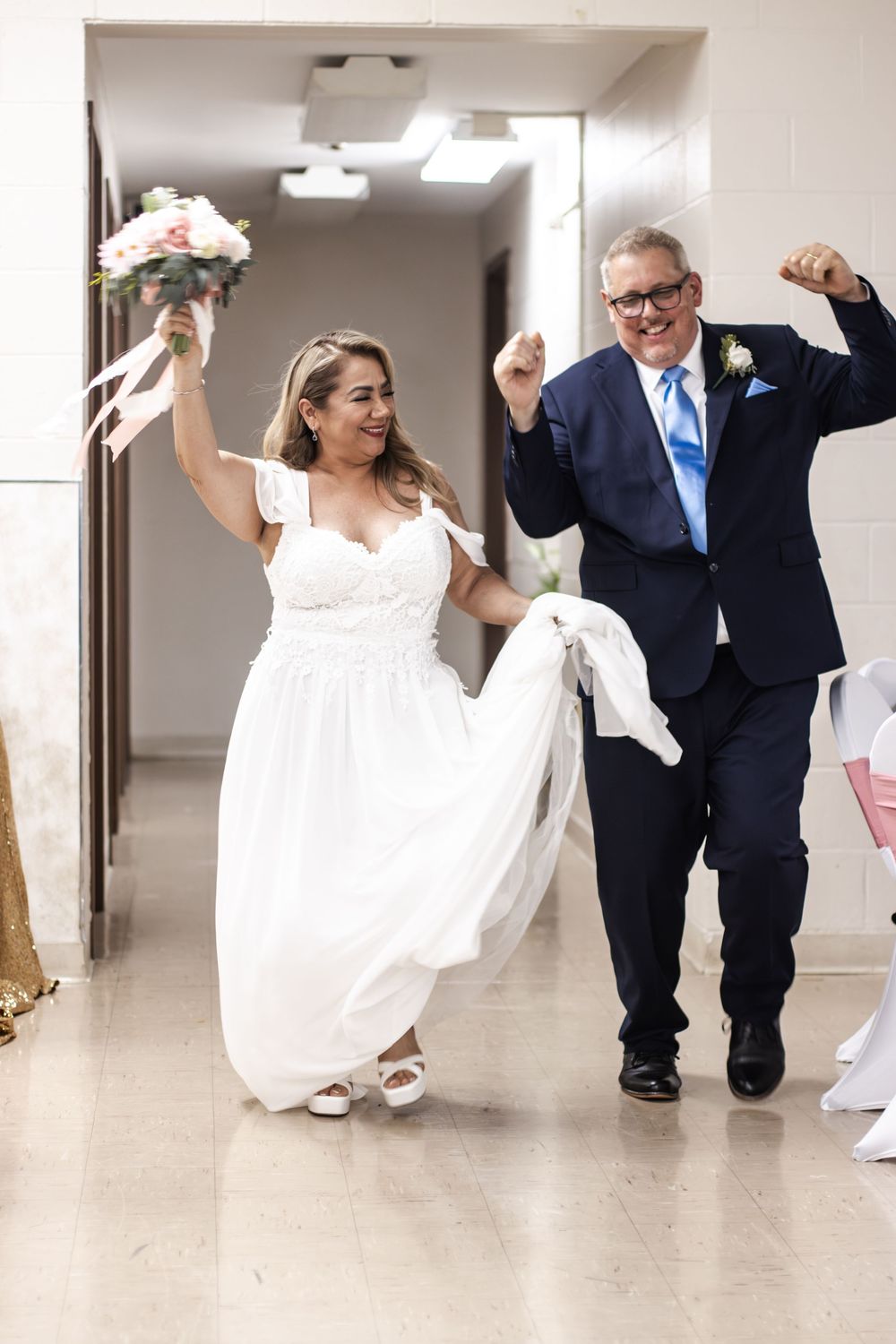 Joyful bride and groom celebrating while walking down hallway after wedding ceremony.