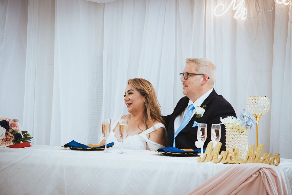Bride and groom seated at sweetheart table with Mr and Mrs sign at wedding reception.