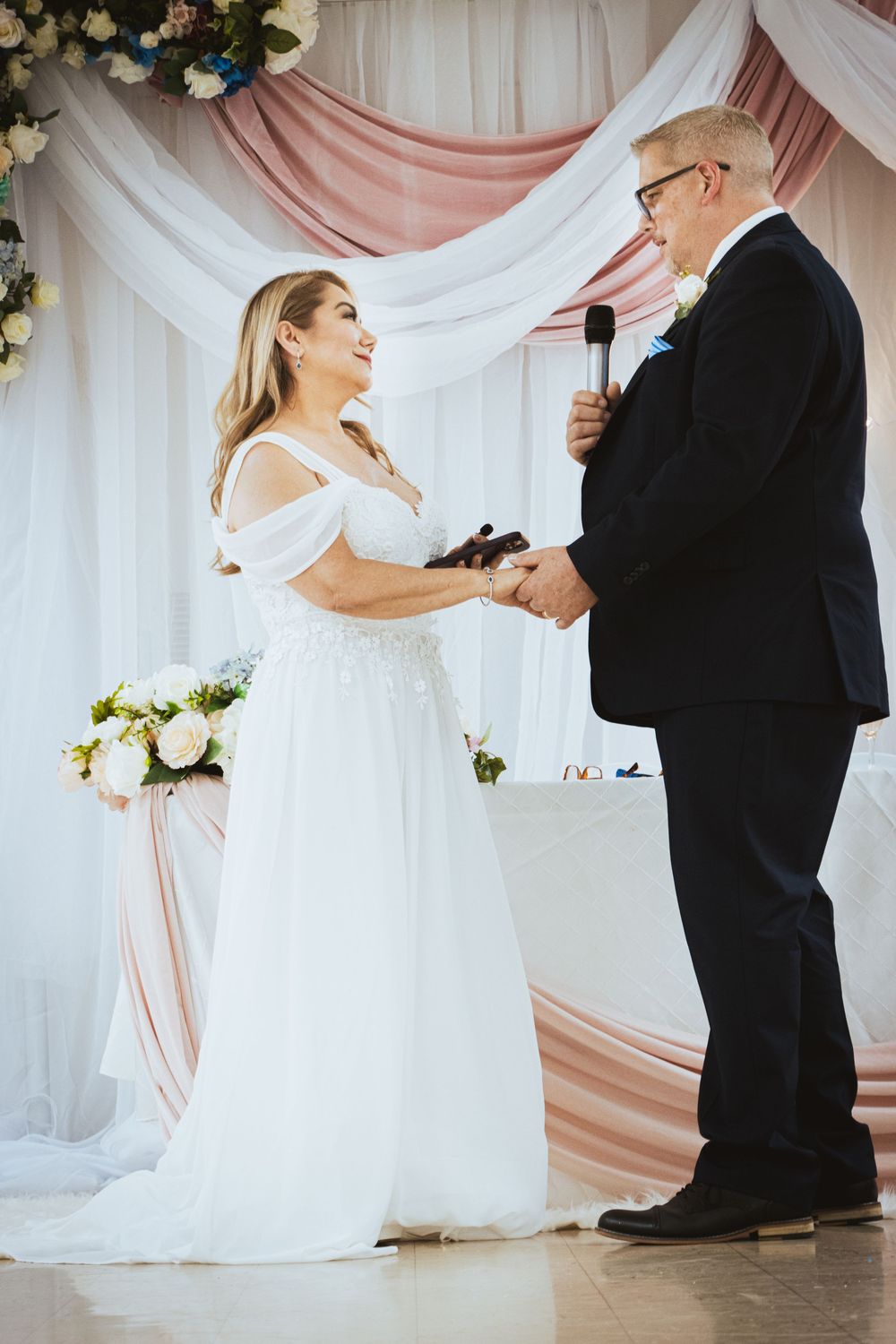 Bride and groom exchanging vows at decorated altar with pink and white draping.
