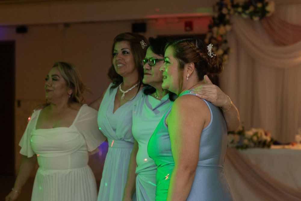 Group of women posing together under colorful lights on wedding reception dance floor.