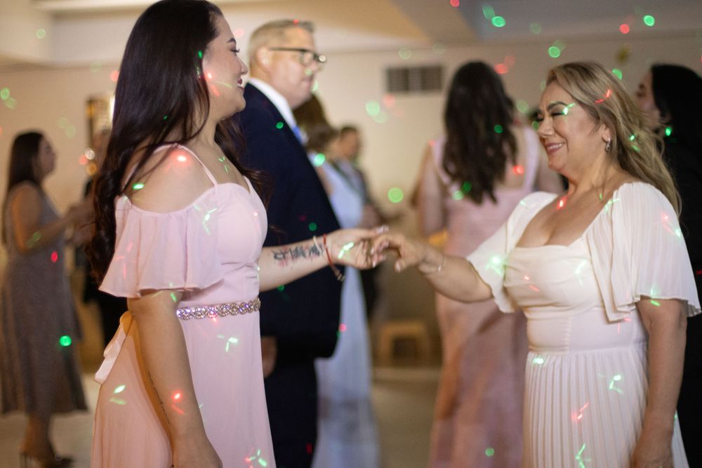Two women in pink dresses dancing together at an elegant wedding reception with colorful bokeh lights.