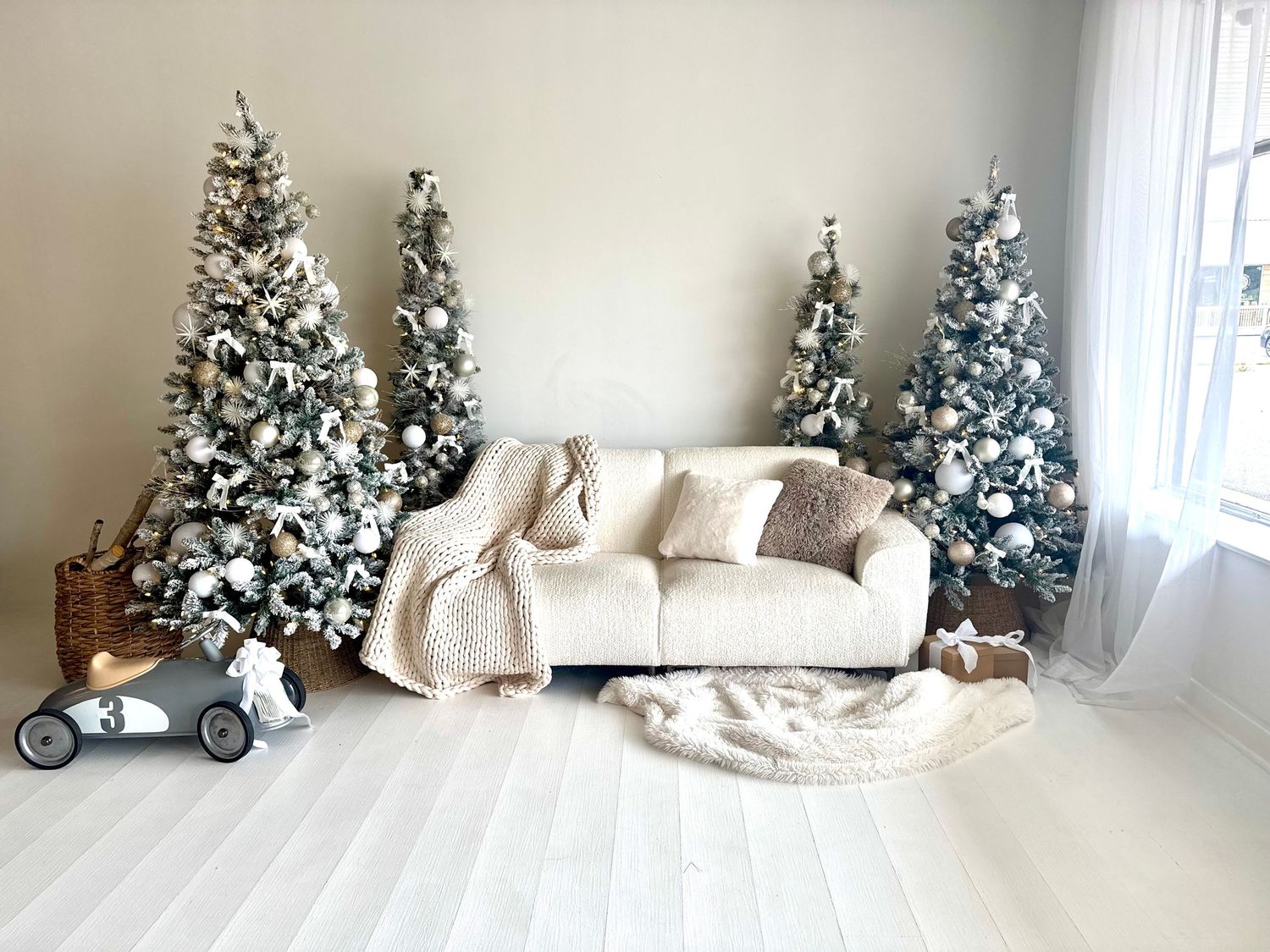 White and gold themed Christmas decorations with multiple trees and neutral decor in a bright minimalist room.