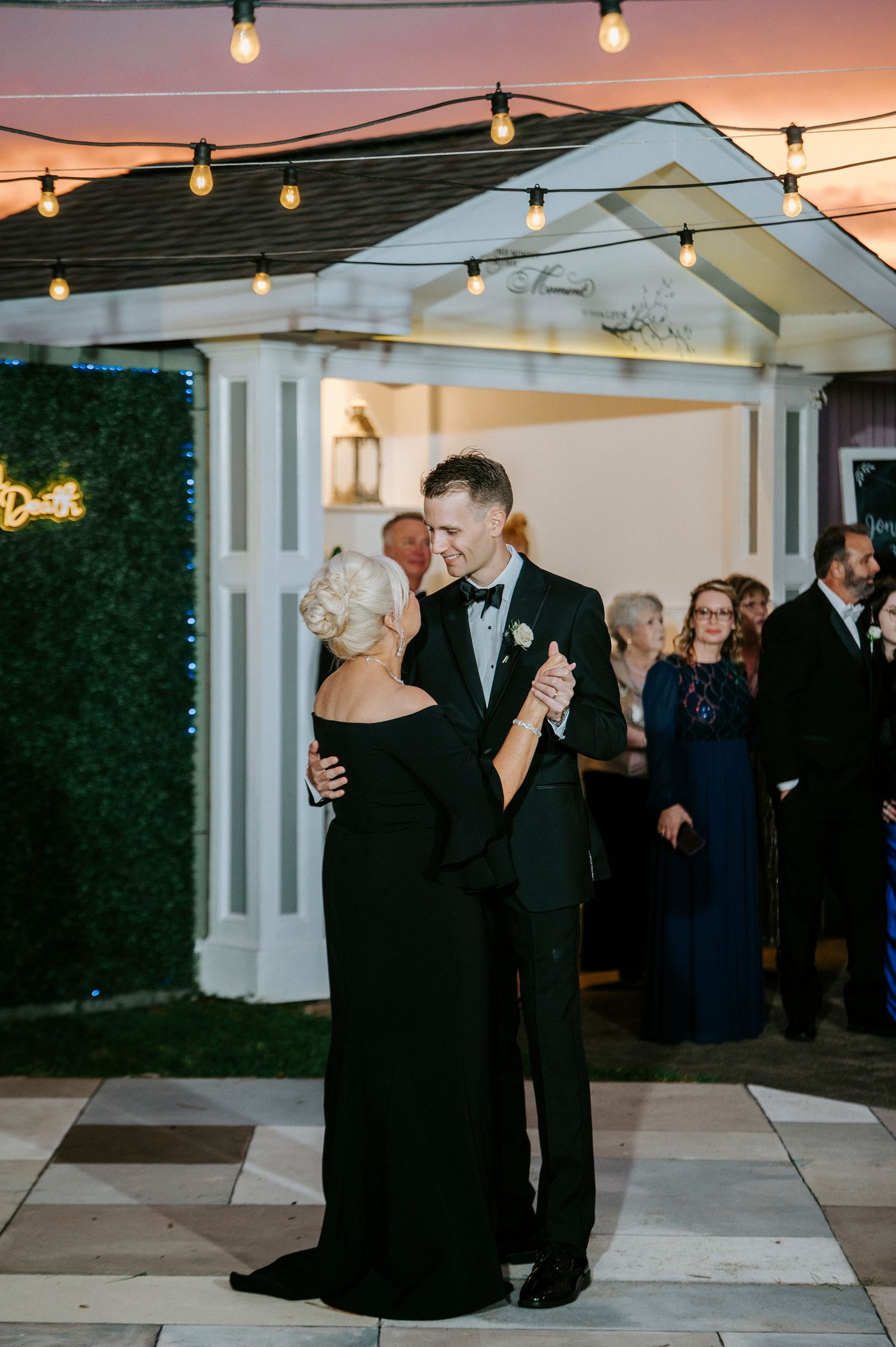 Wedding guests dance under string lights at an outdoor evening reception.