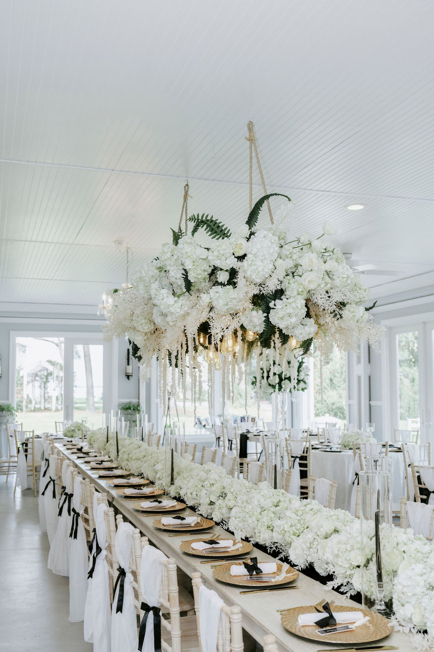 Elegant white wedding reception tables with crystal chandeliers and floral centerpieces in a bright venue.