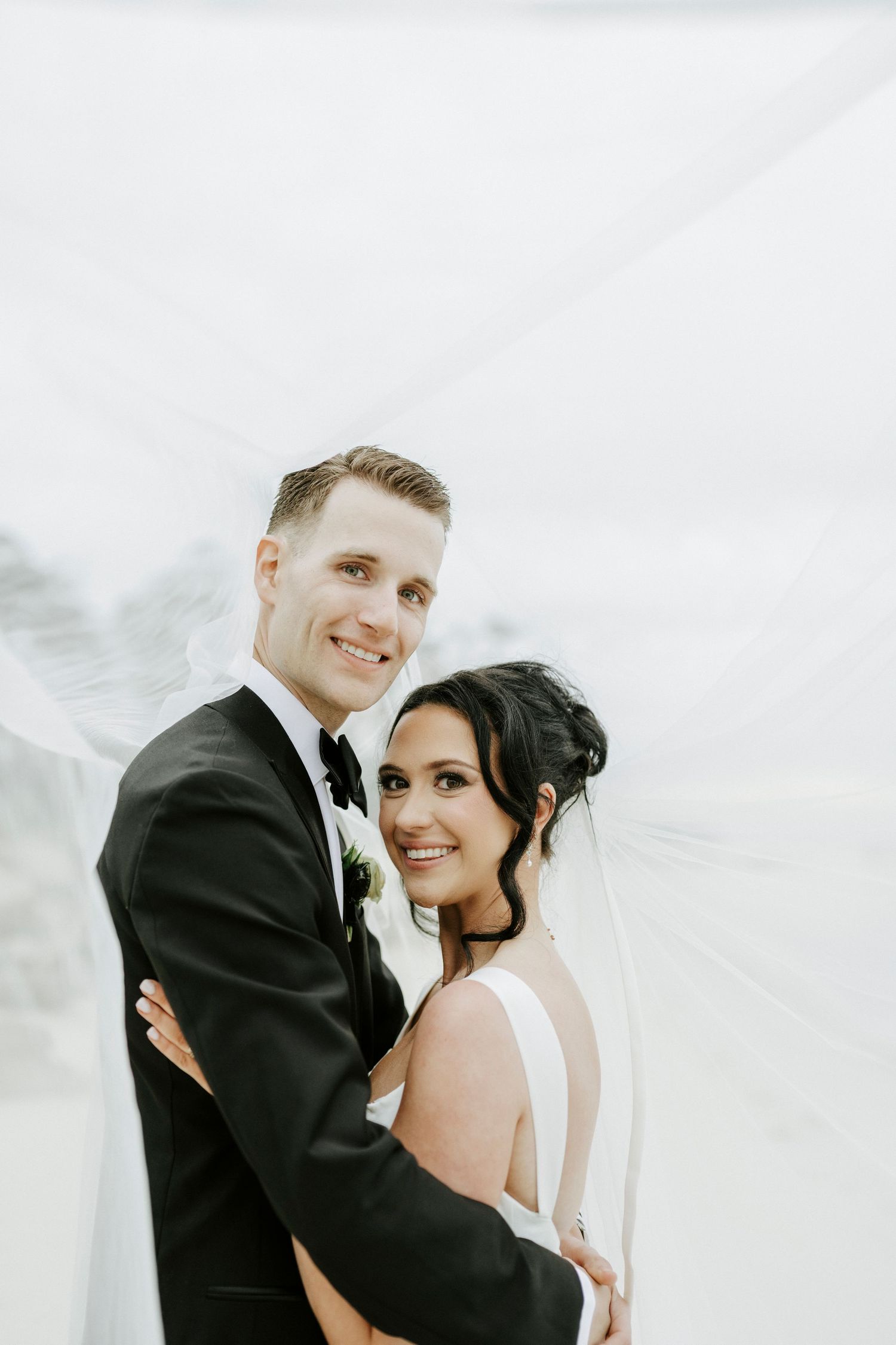 Newlywed couple shares intimate moment against white background during wedding portraits.