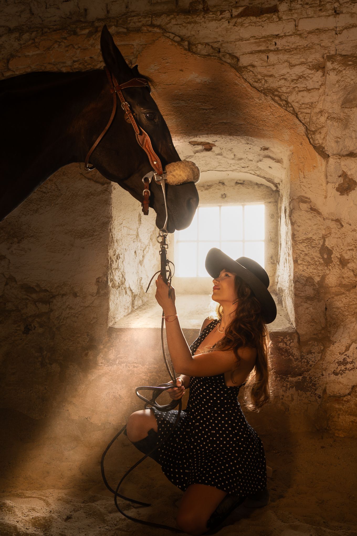 A person in a polka dot dress smokes a hookah pipe in a dimly lit stone room with a small window.